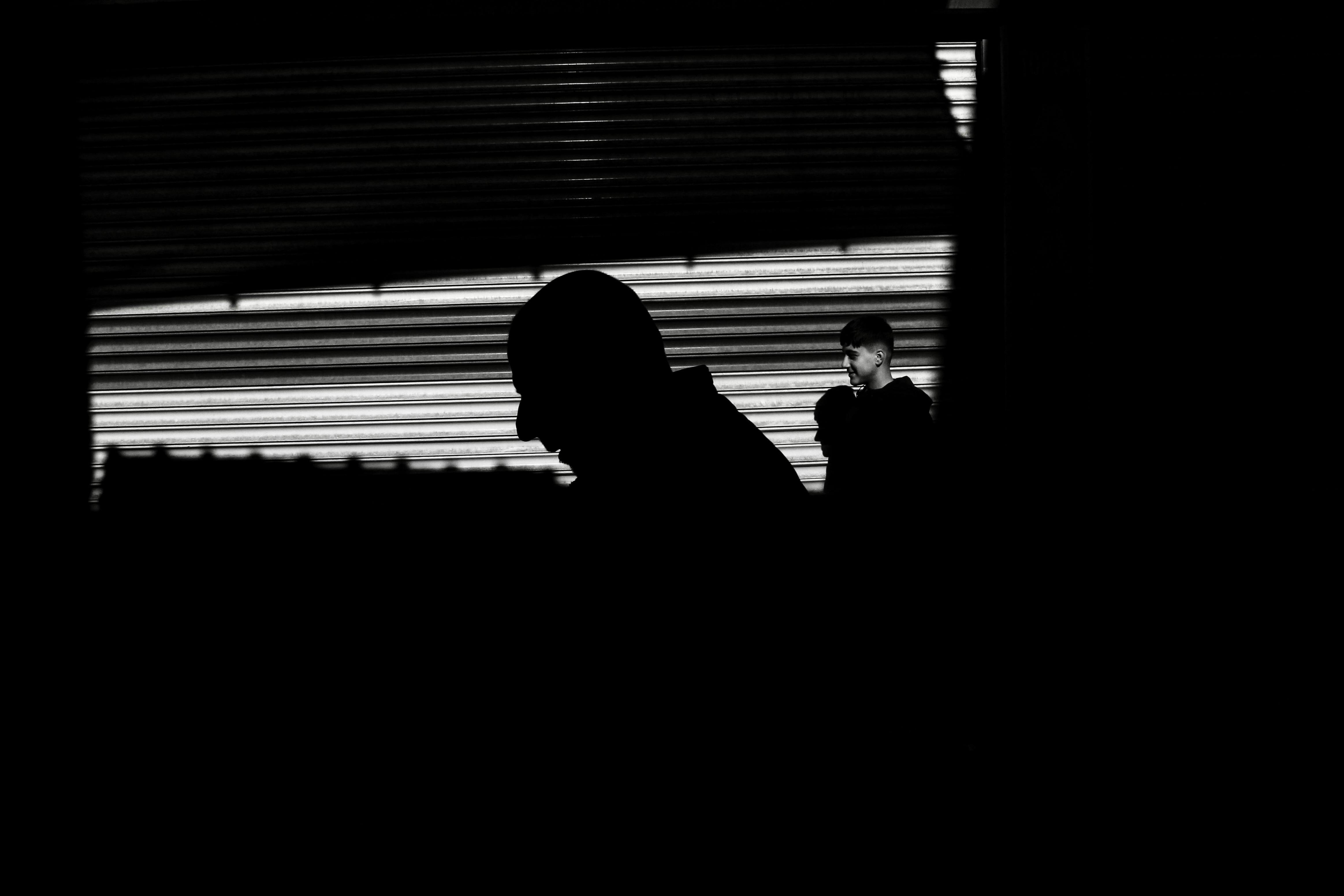 Kostenlos Schwarz-weiße Silhouetten von Menschen im dramatischen Licht der Straßenbeleuchtung. Stock-Foto