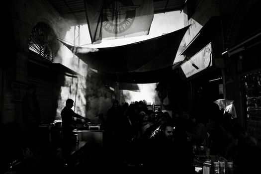 A bustling marketplace in dramatic black and white, showing silhouetted figures against bright light and shadows.