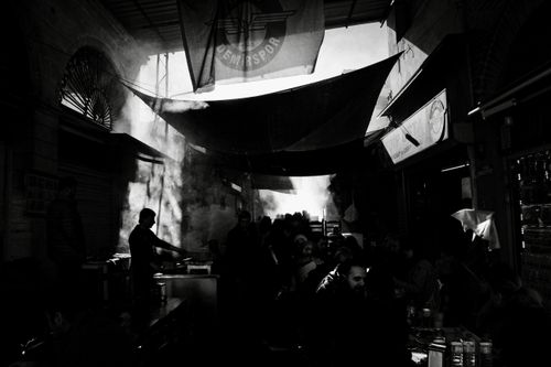 Free A bustling marketplace in dramatic black and white, showing silhouetted figures against bright light and shadows. Stock Photo