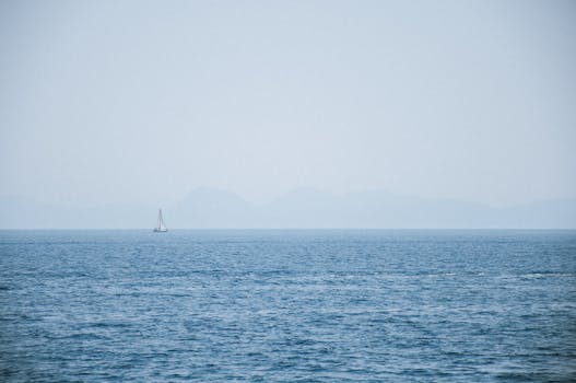 A lone sailboat drifts on calm Aegean waters with distant hazy mountains in Marmaris, Türkiye.