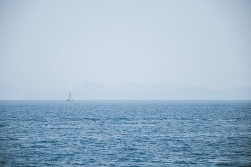 Free A lone sailboat drifts on calm Aegean waters with distant hazy mountains in Marmaris, Türkiye. Stock Photo