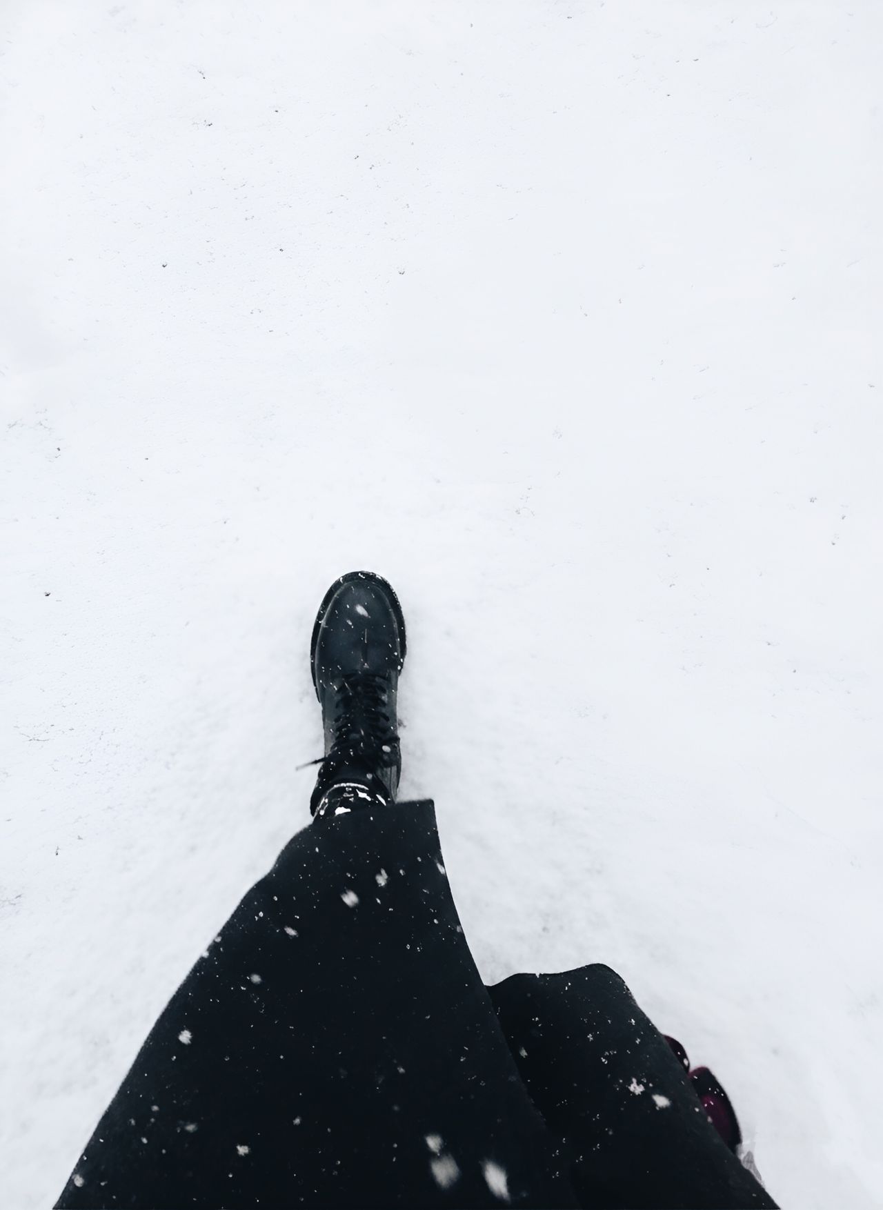 Looking down at a black winter boot stepping into fresh snow
