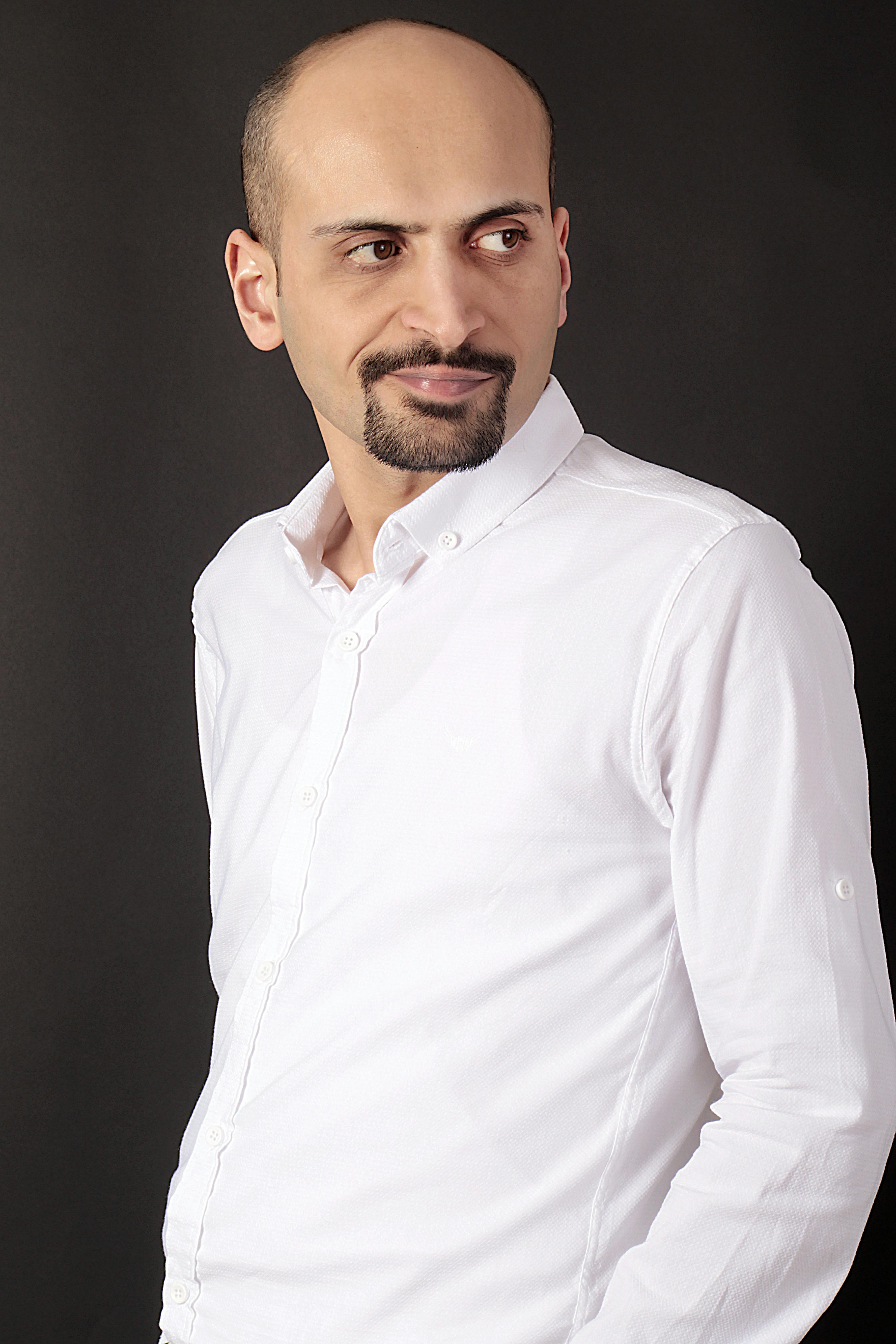 Portrait of a confident man in a white shirt against a dark background, looking sideways.
