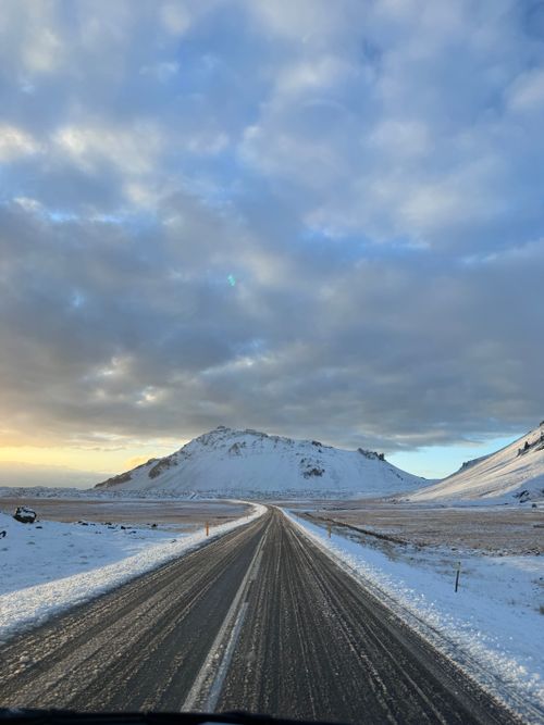 Free A tranquil winter road stretches through Iceland's snowy terrain under a partly cloudy sky. Stock Photo