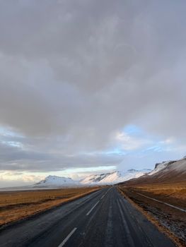 A winter landscape of an empty road leading through snow-capped mountains in Iceland.