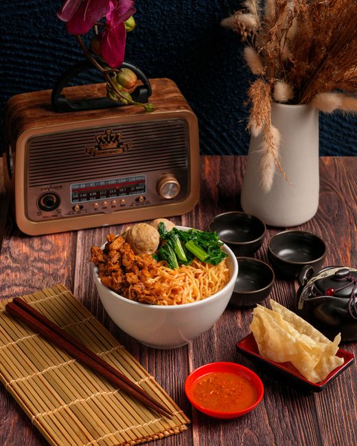 A vibrant noodle bowl with chicken and greens beside a vintage radio and classic decor.