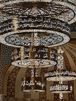 Ornate chandeliers with Arabic calligraphy inside a beautifully decorated mosque.