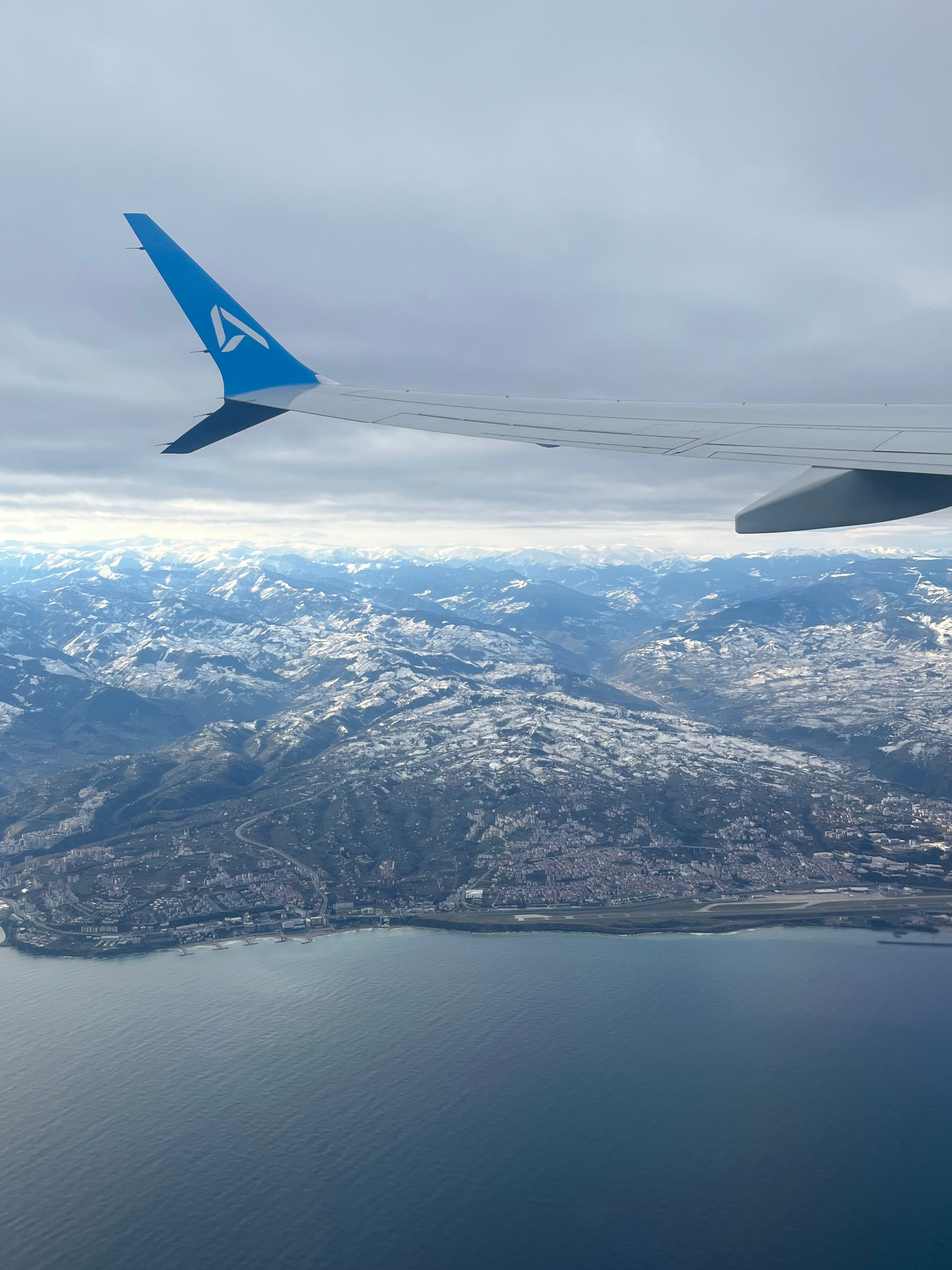 Breathtaking aerial view of snowy mountains and ocean captured from an airplane window.
