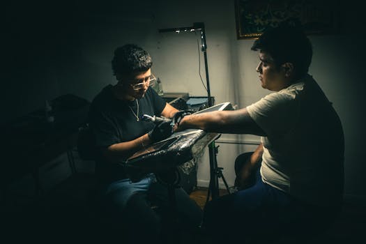 Artist tattooing a client in a dimly lit studio, capturing the intimacy and craftsmanship of the tattooing process.