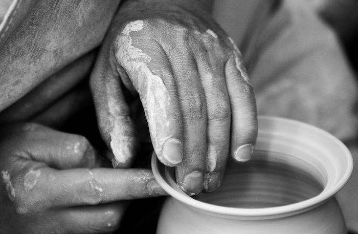 Hands shaping a clay pot on a wheel, black and white