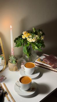 Warm indoor setting with coffee, flowers, and candle creating a cozy atmosphere.