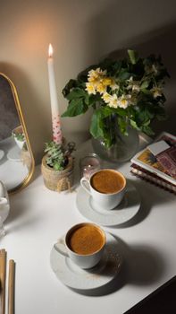 Warm ambiance with coffee cups, flowers, and candlelight on a table.