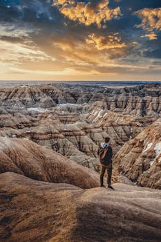 A lone traveler stands atop rugged badlands under a striking sunset sky, capturing the essence of exploration.