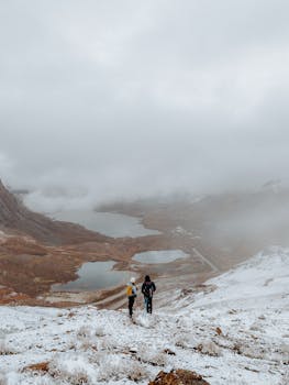 Two hikers traverse a snowy mountain landscape under a cloudy sky, exploring nature.