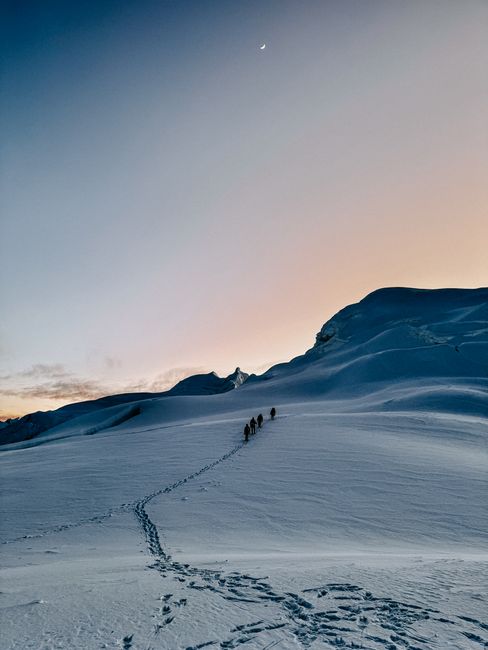 Group of climbers ascending a snowy mountain at dawn, with a serene sky.