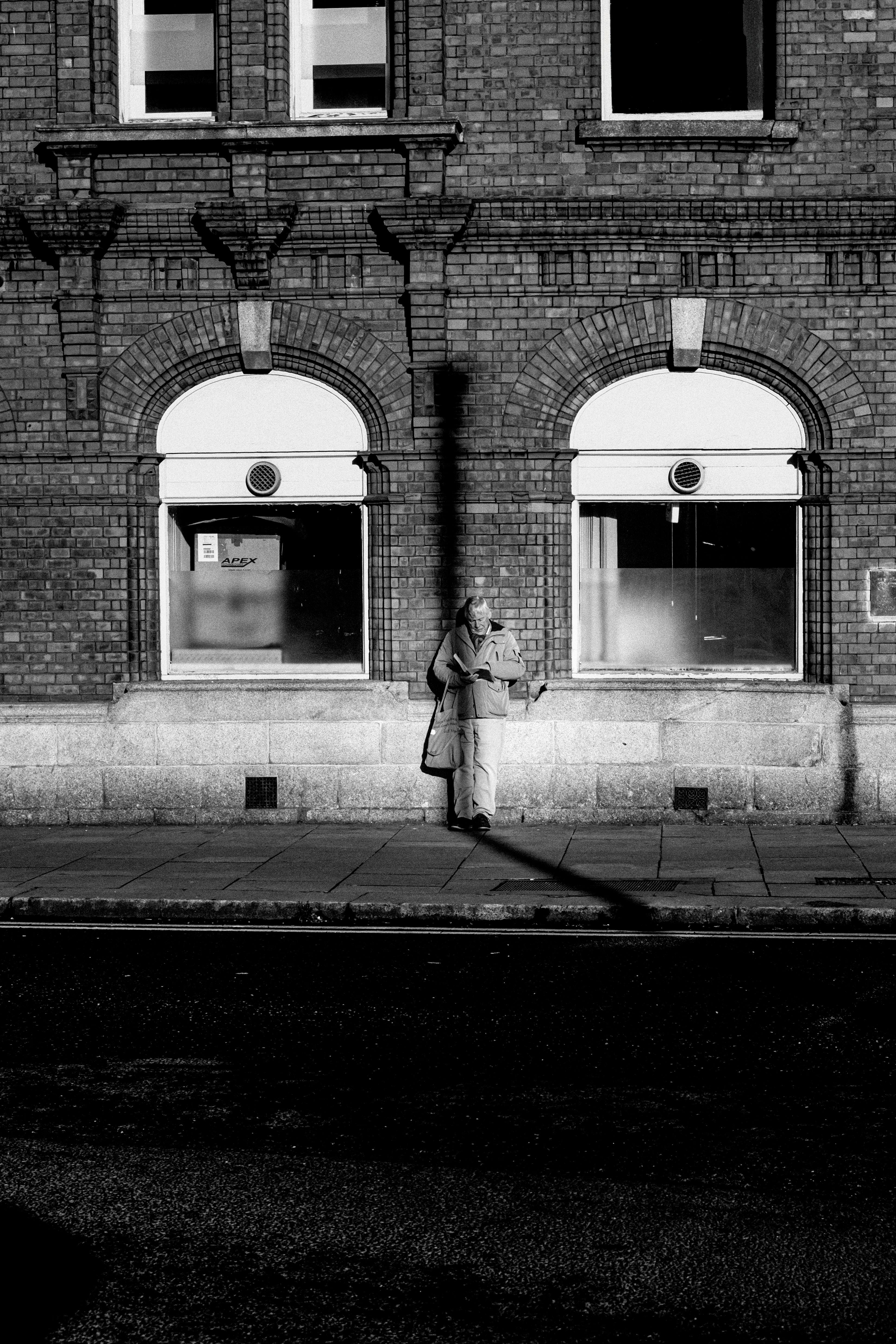 Free A solitary figure stands by a brick building in Dublin, captured in monochrome. Stock Photo
