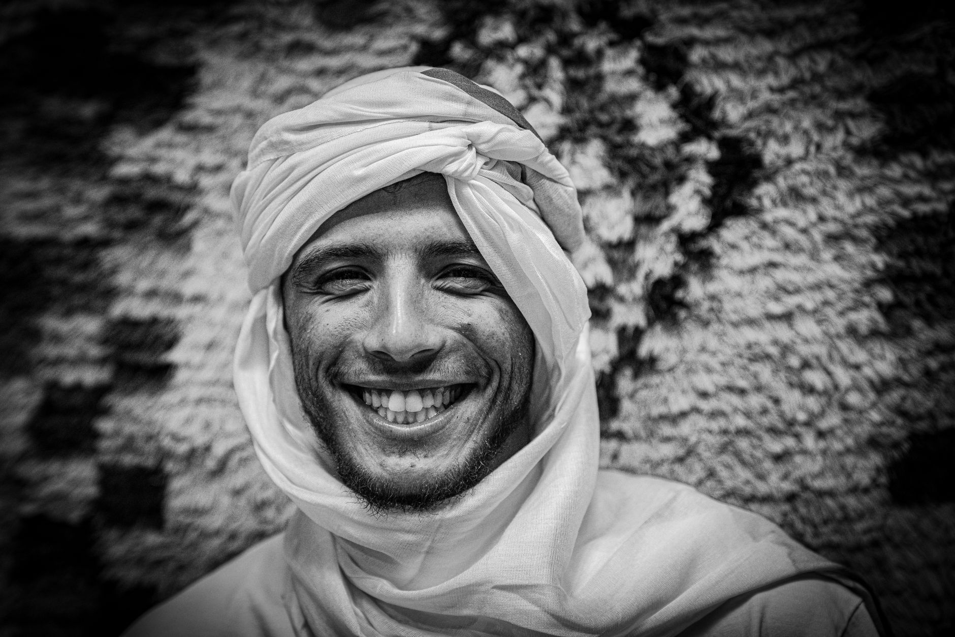 Black and white portrait of a man wearing a traditional headscarf, smiling warmly.