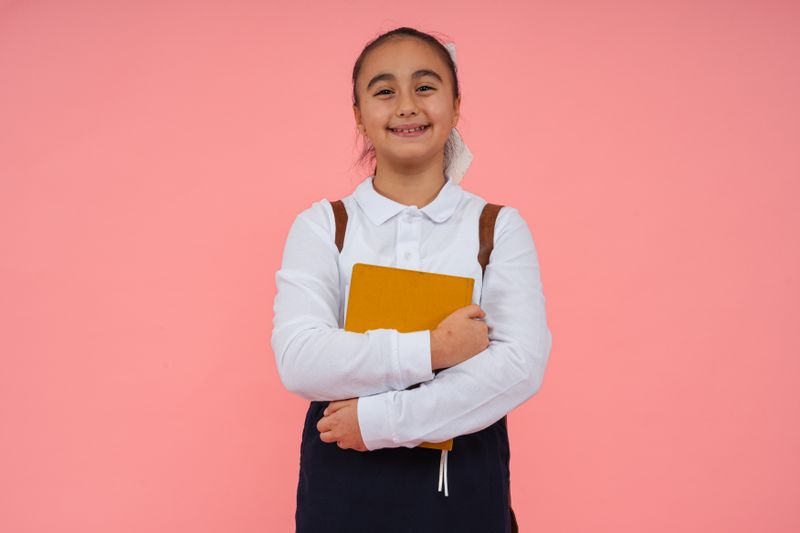 A cheerful schoolgirl holding a book against a bright pink background, symbolizing education.