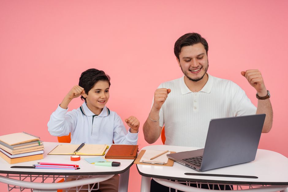 Father and son joyfully celebrate finishing homework together on a laptop.