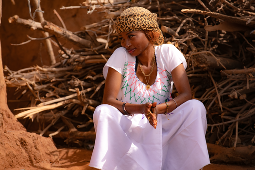 A woman wearing a traditional dress and leopard print scarf sits outdoors in a sunny setting.