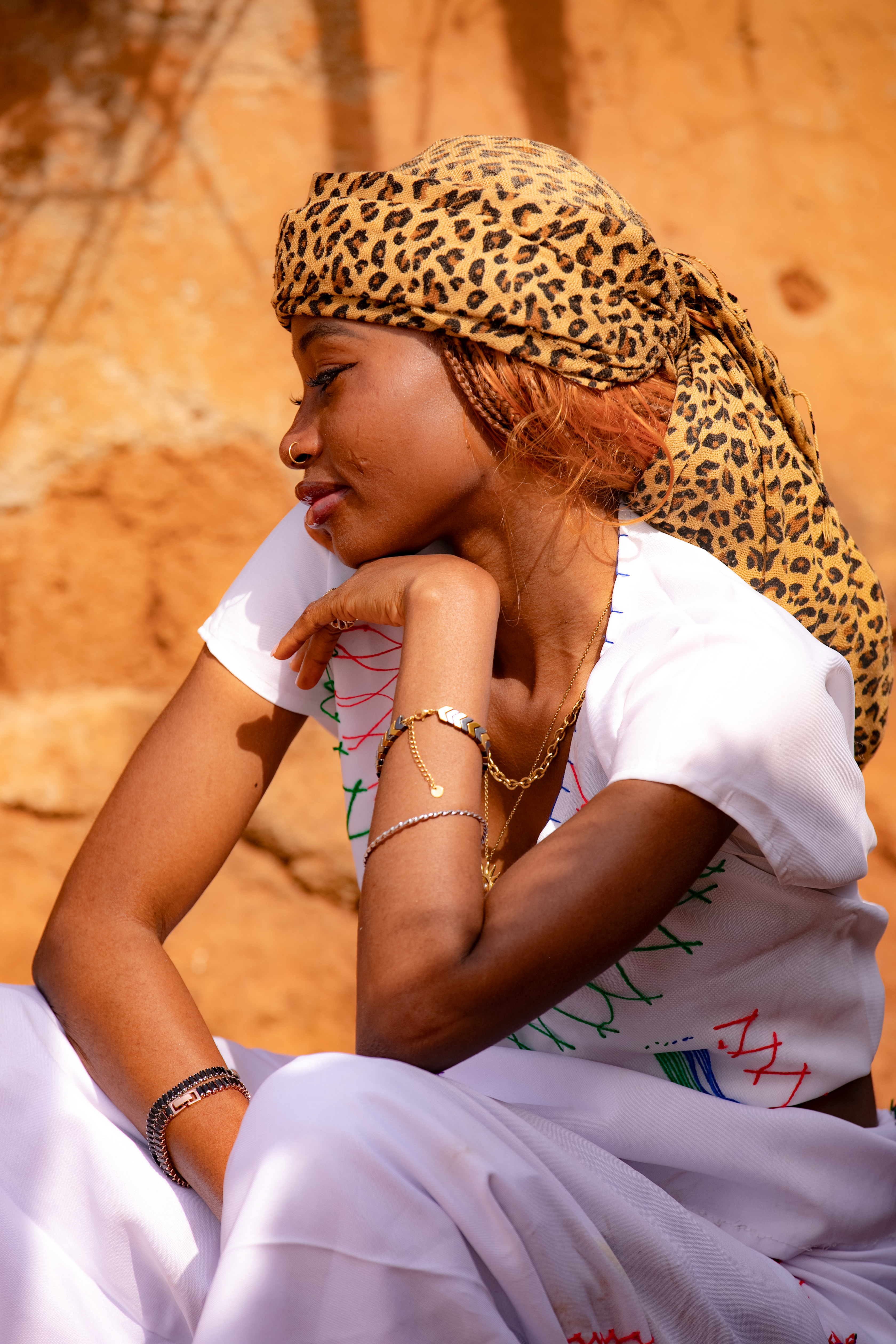 A young woman in traditional attire sits thoughtfully against an earthy background.
