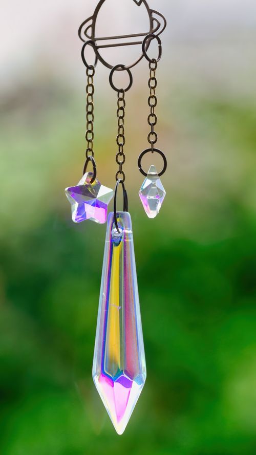 Free Vibrant crystal prisms and star charm hanging against a blurred green background, creating a rainbow effect. Stock Photo
