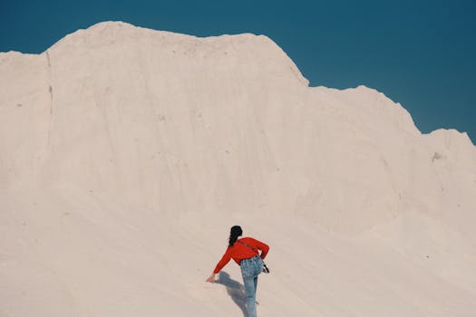 A person in red jacket climbing picturesque white sand dunes under a clear blue sky in Egypt.