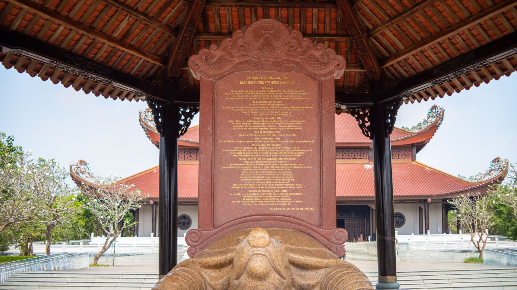 Stone tablet and statue in a Vietnamese temple, showcasing intricate architecture under a clear sky.