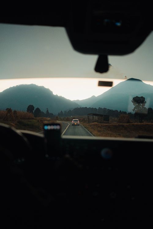 Free View through car windshield of a road leading towards mountains at dusk, capturing serene and adventurous vibe. Stock Photo