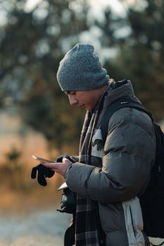 Young man in winter clothing using smartphone outside during the day.
