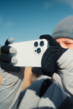 Person wearing gloves and beanie taking a photo with smartphone in cold weather.