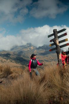 Adventurous hikers on a mountainous trail with a vibrant directional signpost under a blue sky.