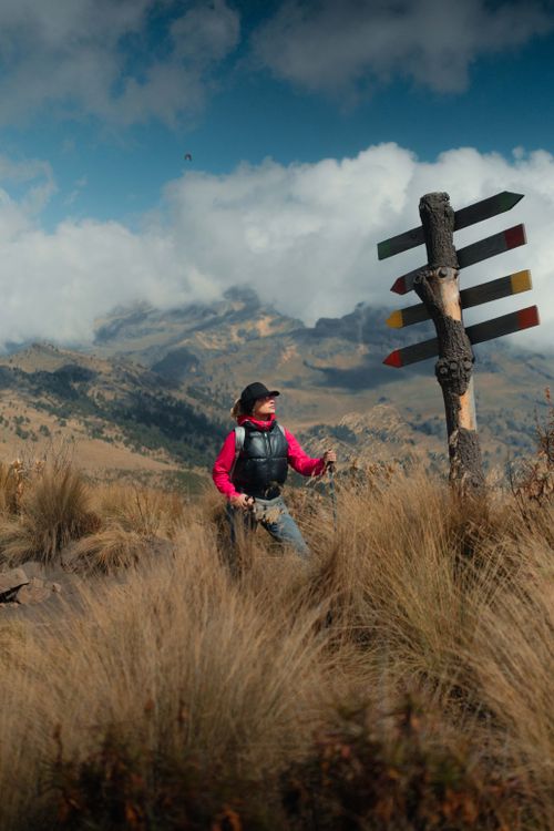 Free A woman in hiking gear exploring a mountainous landscape with a colorful signpost and dramatic skies. Stock Photo