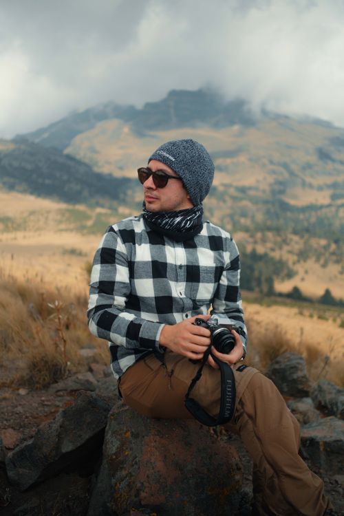 Free Man in casual attire holding camera in a picturesque mountain setting. Stock Photo