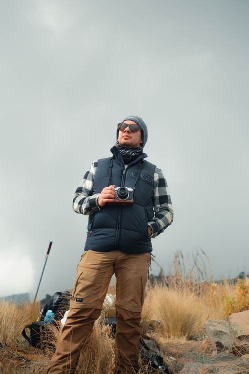 Free A photographer stands in an outdoor mountain landscape, holding a camera and dressed warmly. Stock Photo