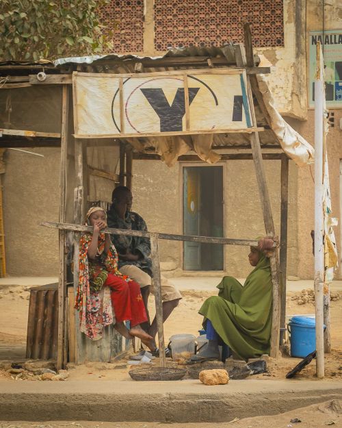 Free Group of people gathered at a small market stall in a dusty street, engaging in conversation and daily activities. Stock Photo