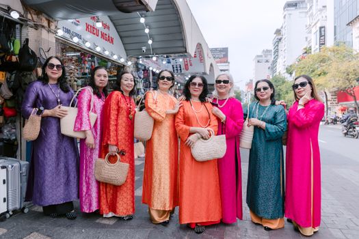 Women in colorful Ao Dai fashion pose in urban cityscape, smiling.