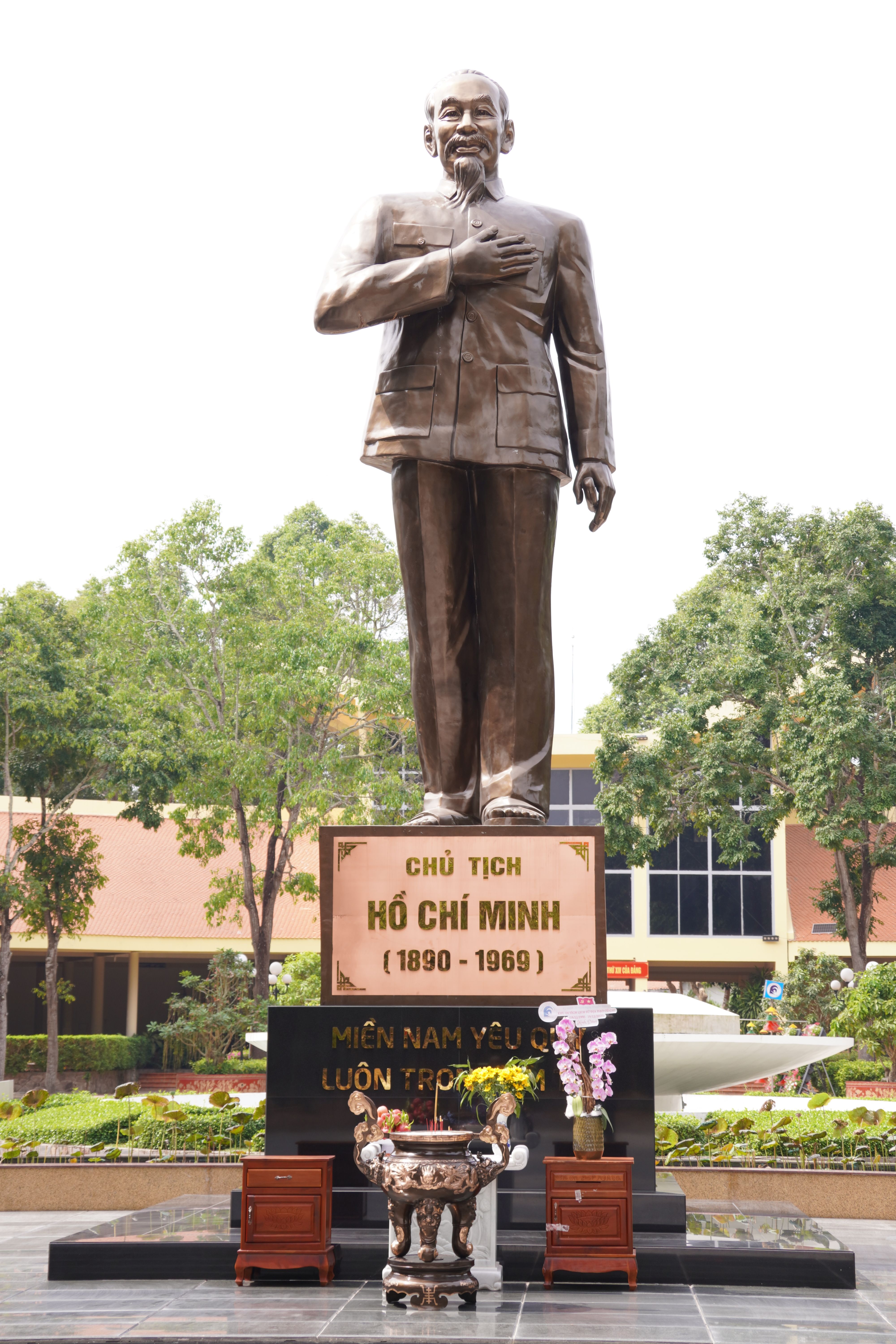 Statue of Ho Chi Minh in a park, surrounded by greenery and urban architecture.