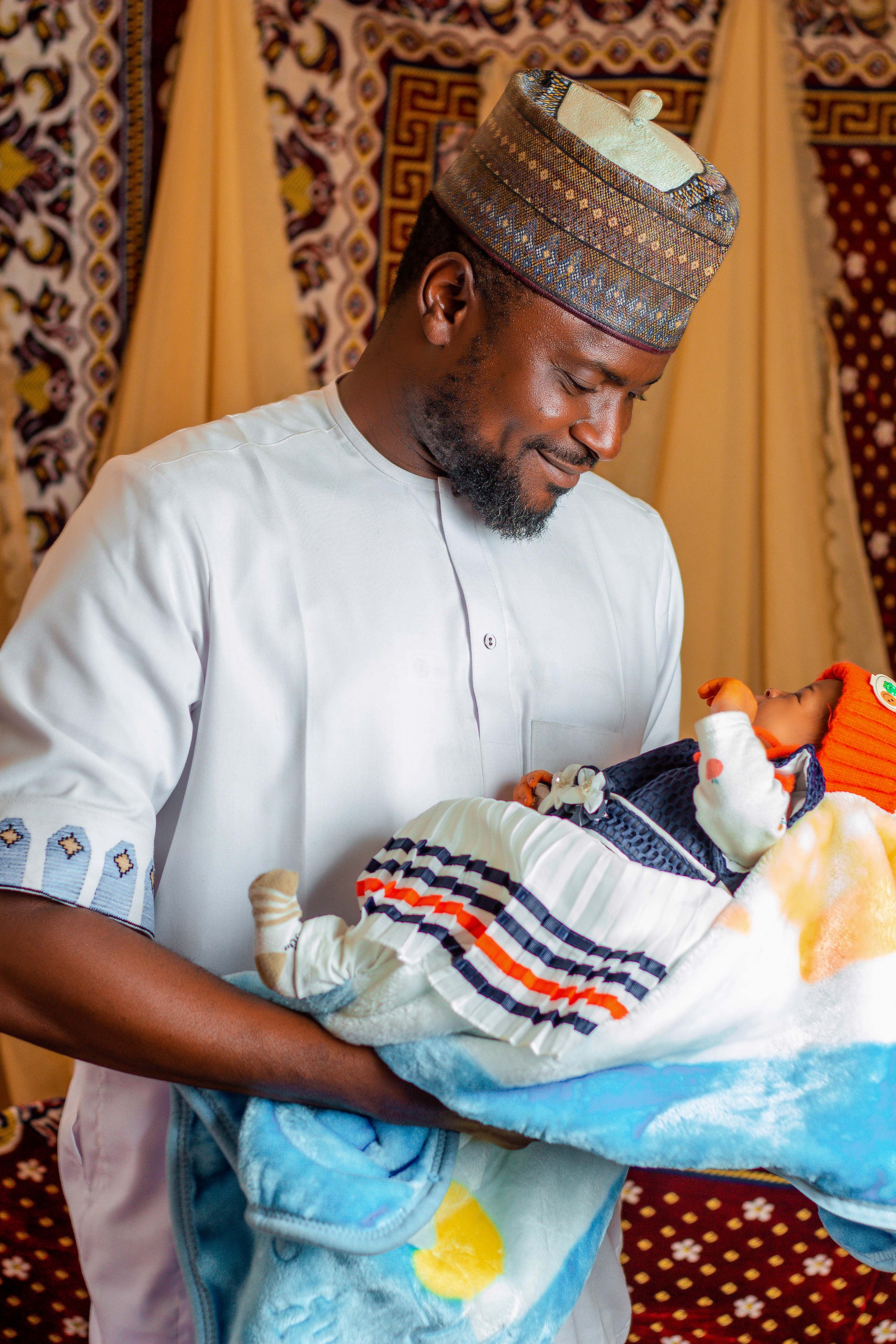 A joyful father holds his newborn baby lovingly, dressed in traditional vibrant clothing.