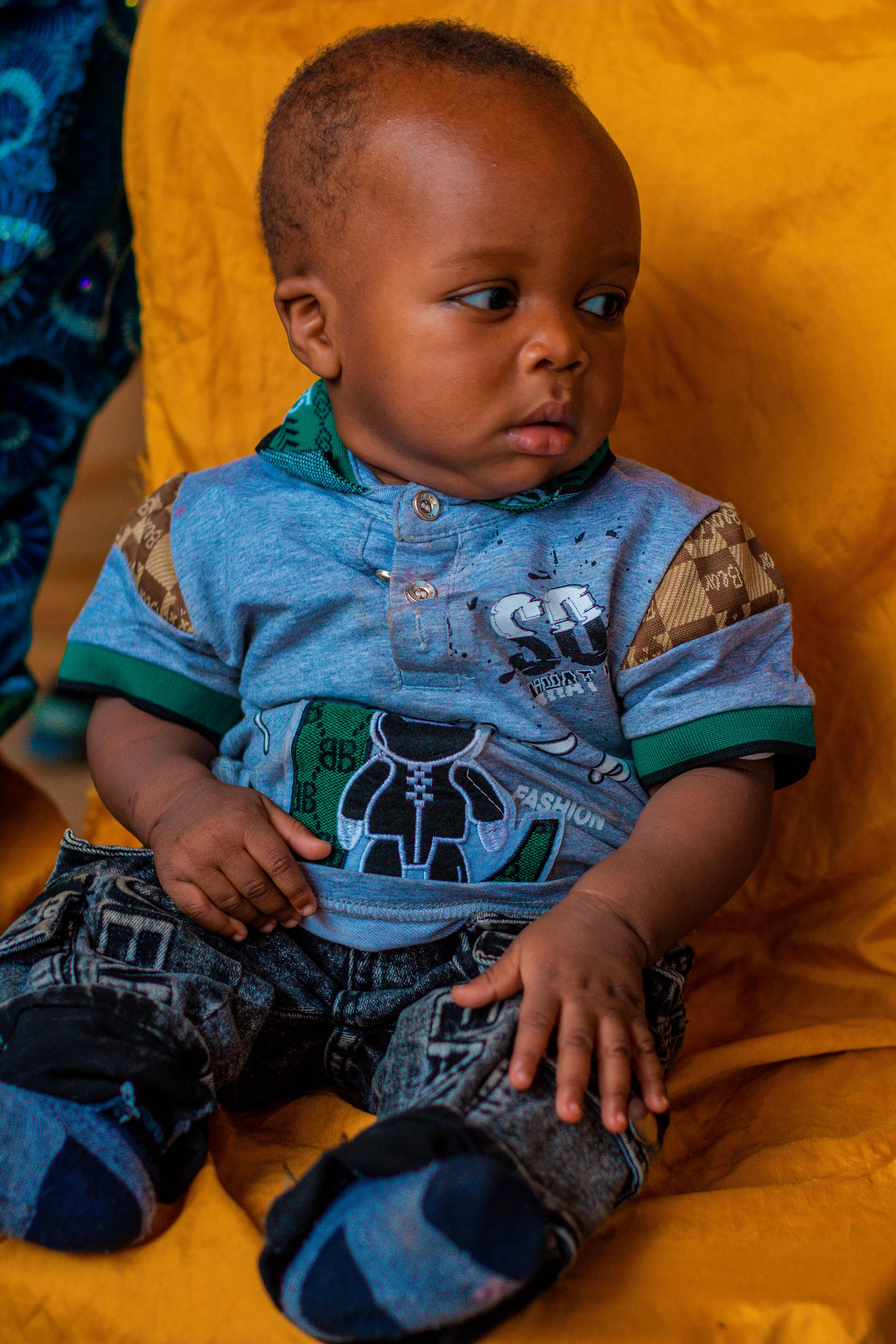 Cute baby wearing casual clothes sitting on a vibrant fabric background.