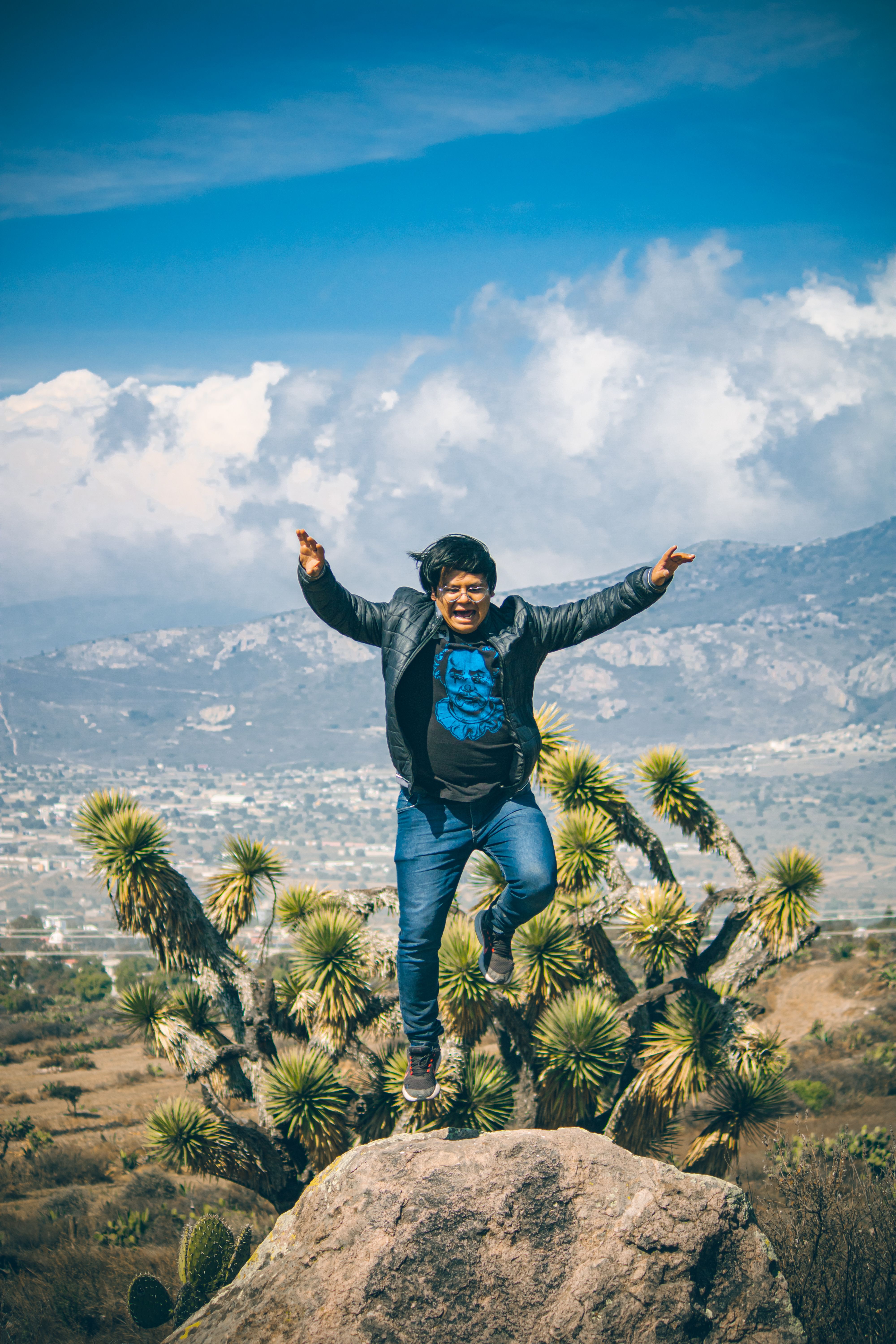 A man joyfully jumps on a hilltop with a scenic Mexican backdrop.