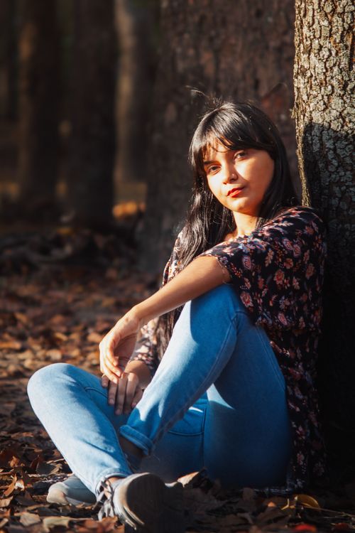 Free A young woman with long hair sitting by a tree, enjoying the natural forest scenery. Stock Photo