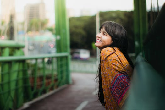 A young woman smiles brightly while leaning on a green bridge in a vibrant city setting.
