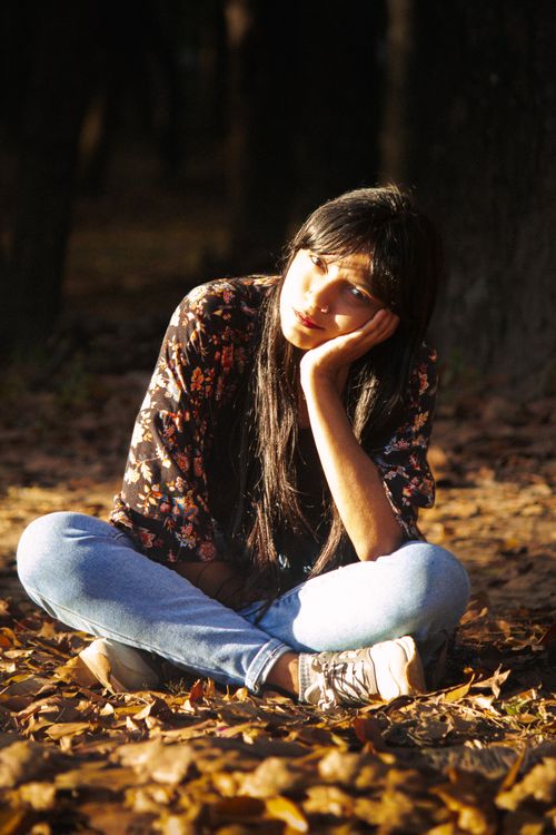 Free A pensive woman sits cross-legged among fallen leaves in a sunlit forest. Stock Photo