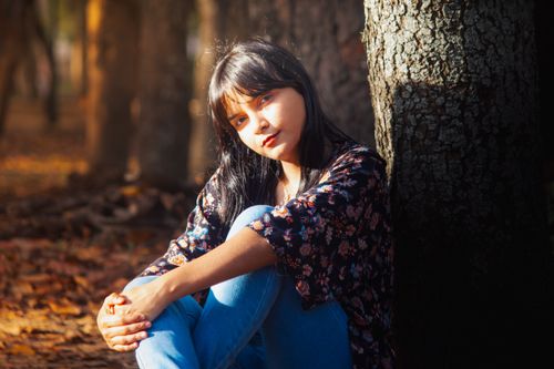 Free A serene portrait of a young woman sitting in a sunlit autumn forest, capturing nature's tranquility. Stock Photo