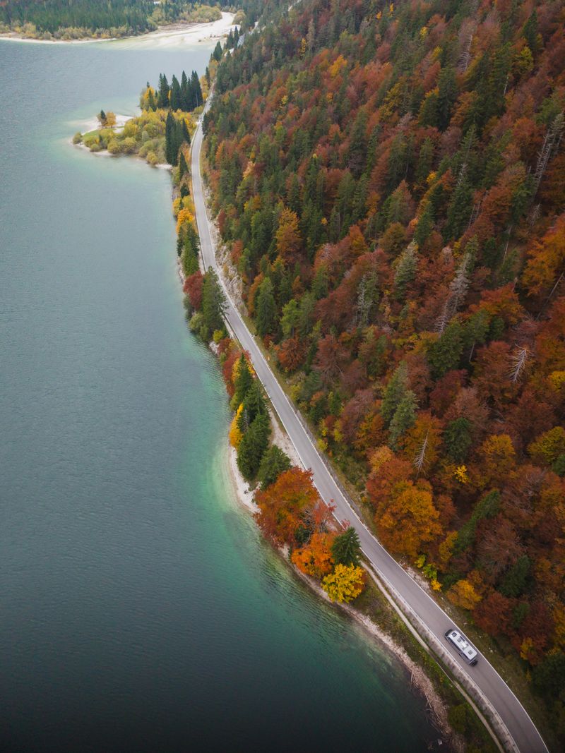 Aerial view of picturesque autumn lakeside road surrounded by colorful foliage.