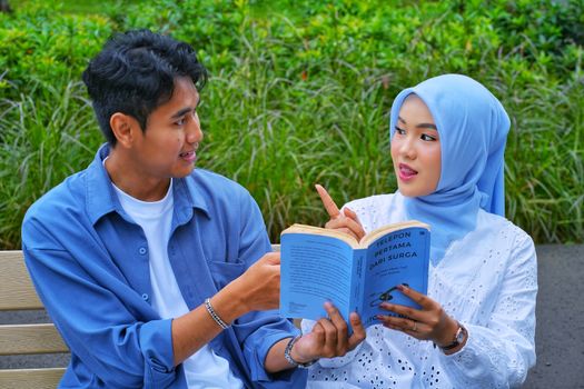 Young couple enjoying a lively reading session in a park, discussing a book.
