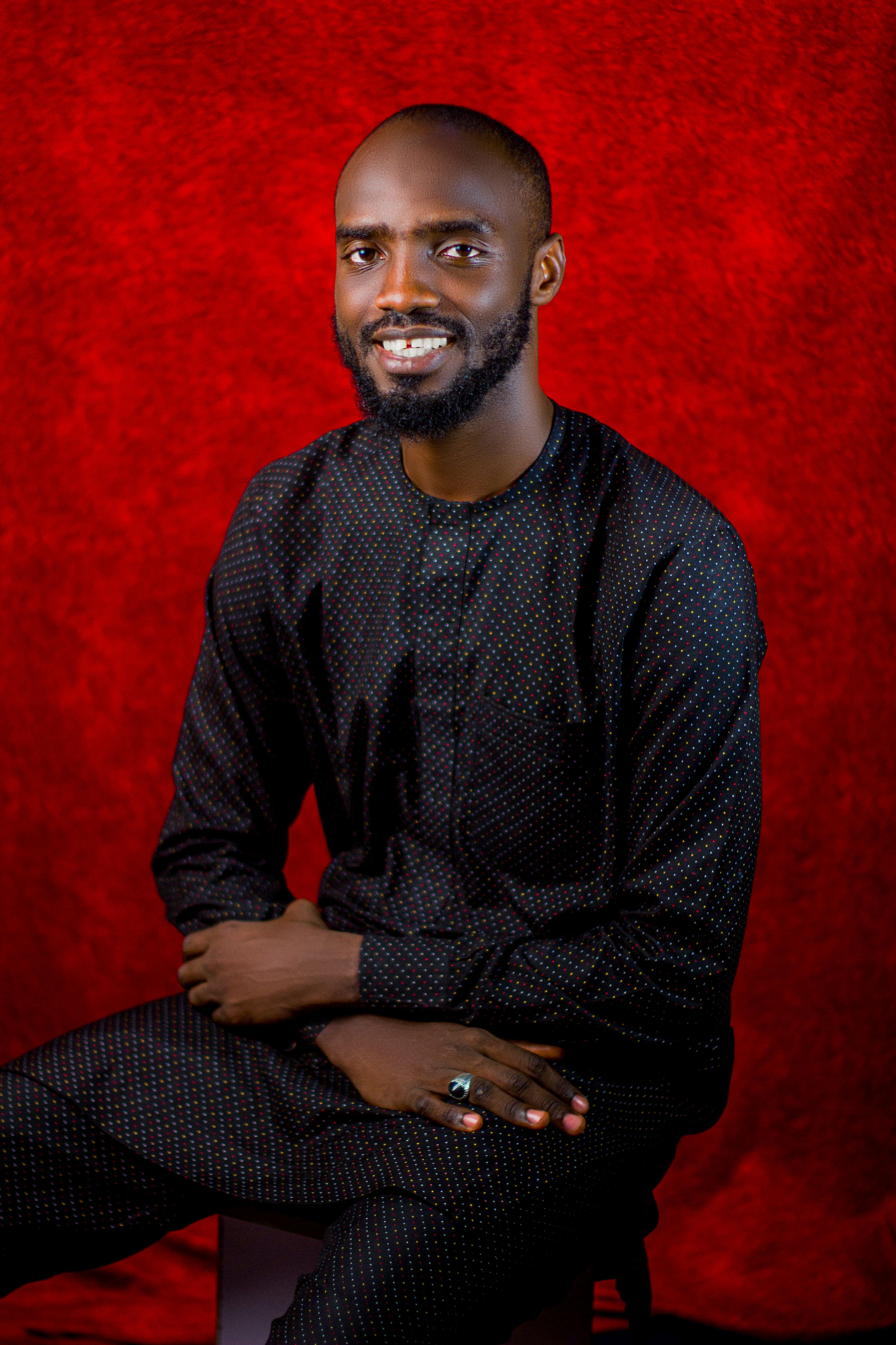 Portrait of a smiling man in traditional attire against a deep red background.