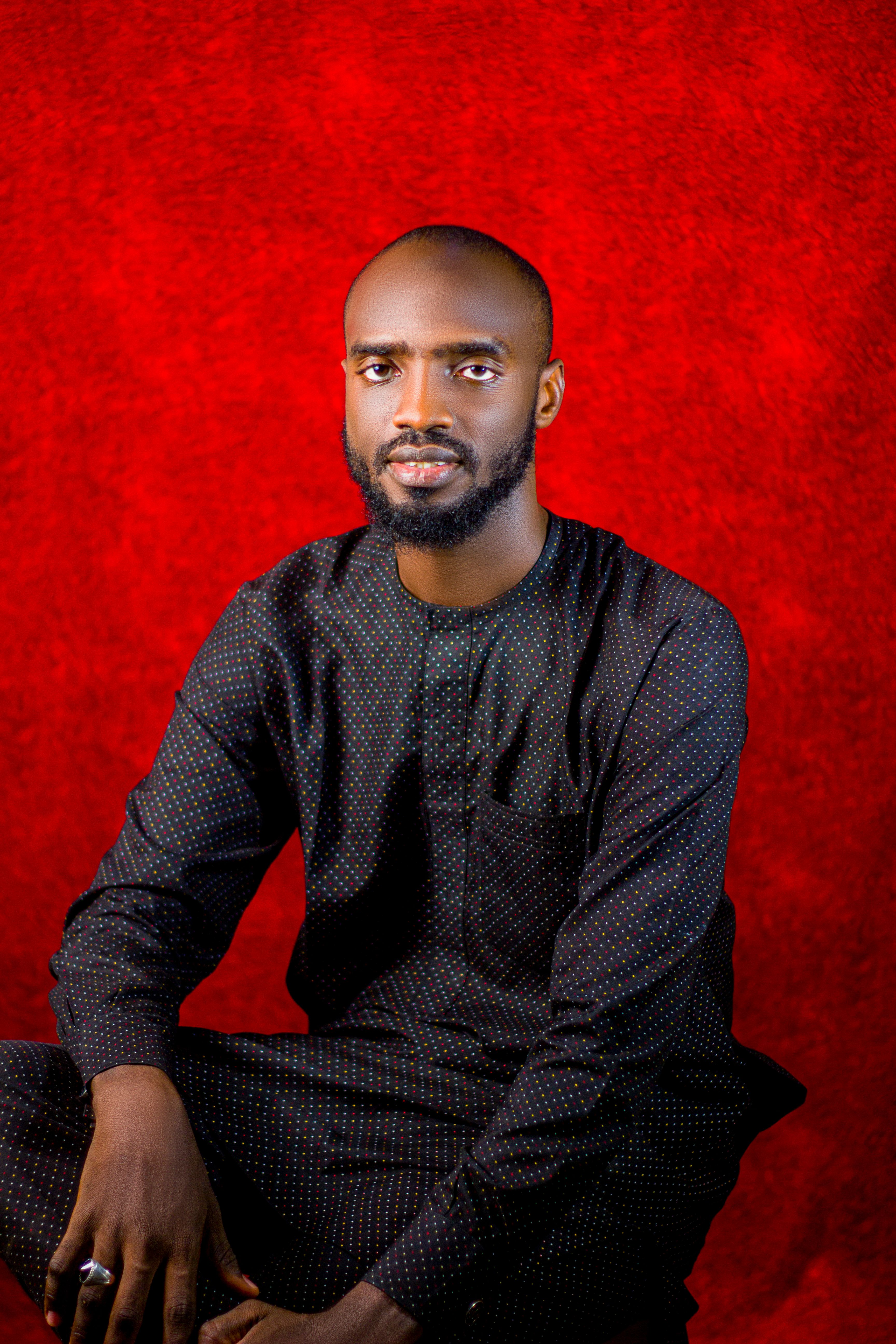 Portrait of a man in a black outfit against a vibrant red background.