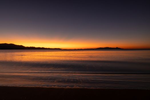 Peaceful sunset over calm sea with distant mountains silhouetted.